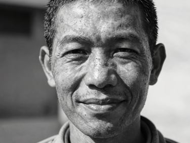 Close-up black and white portrait of an educator smiling gently, natural outdoor lighting, raw texture, high contrast.