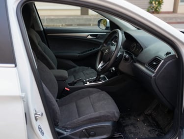Close-up of a vacuumed and conditioned car interior, dark seats with no debris, dashboard wiped clean, shot from the open driver door in daylight showing the full front cabin