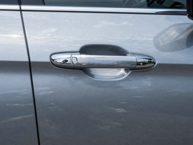 Tight close-up of a freshly detailed car door panel in clear daylight, glossy paint surface reflecting light, clean seam and chrome trim visible, no people