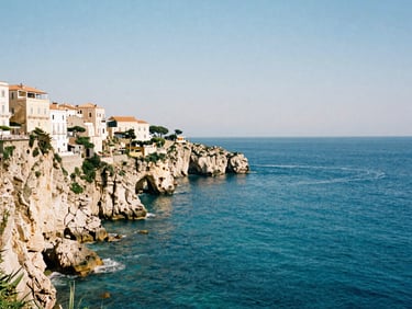 Dramatic coastal cliffs of Tropea with historic buildings perched on top, viewed from the deep blue sea, bright daylight