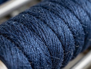 Macro close-up of dense indigo cotton threads aligned on an industrial warp beam, natural side-lighting emphasizing tactile fiber texture, shallow depth of field