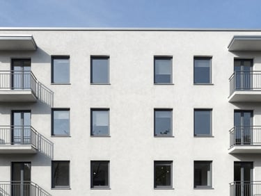 Straight-on architectural shot of a renovated multi-family apartment building in Göttingen, clean gray facade, bright daylight, sharp focus, 35mm lens