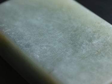 Close-up of smooth jade-toned stone surface, cool diffused studio light, fine grain and mineral variation visible, quiet empty composition
