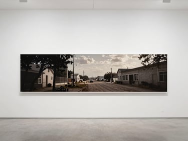 Wide panoramic photograph of a large-format archival pigment print from the 'Industrial Scars' series, mounted on a clean white gallery wall, soft diffused daylight.
