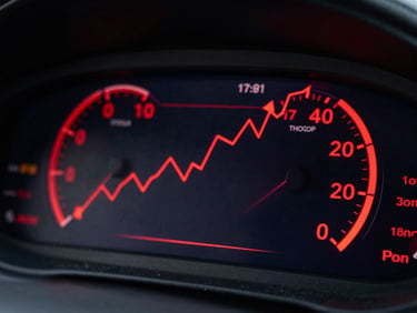 Moody high-contrast close-up of a digital dashboard on a screen in a dark room, glowing red metrics and trend lines pointing upward, sharp angles.
