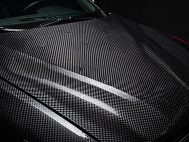 Macro shot of a carbon fiber texture vinyl wrap on a car hood, dramatic studio lighting, 50mm