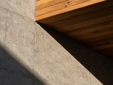 Architectural close-up of raw textured concrete and warm wooden slats under the high-contrast late afternoon Paracas sun, geometric shadow patterns.