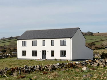 Wide environmental shot of a new-build rural dwelling set into a hillside, clean rendered walls, UK countryside backdrop, flat even north-facing light