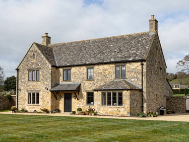 Wide exterior shot of a stone farmhouse with a new rear extension, clean architectural lines, UK rural setting, overcast bright daylight