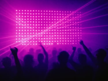 Motion-blurred crowd silhouette against a massive wall of purple strobe lights, heavy grain, raw club atmosphere