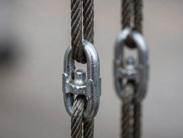 Close-up macro shot of heavy steel rigging cables and shackles locking onto a load, tension visible, cold metallic texture.
