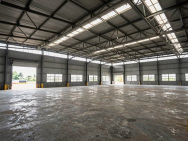 Wide interior shot of a large clear-span warehouse in Auto Nagar industrial corridor, Vijayawada, concrete floor, steel truss roof, loading bay doors open at far end, natural light spilling in