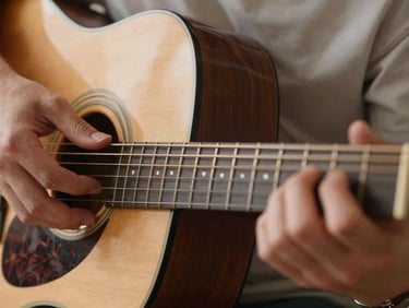 Close-up of acoustic guitar frets with hands positioning a chord, warm natural light, editorial photography.