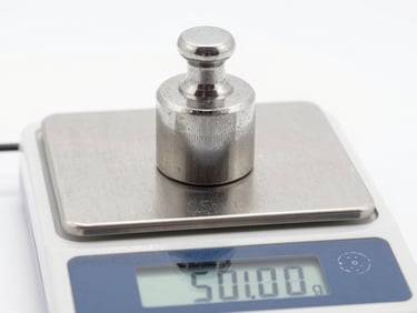 Macro shot of a high-precision stainless steel calibration weight sitting on a digital scale display showing exactly 500.00g, bright clinical white lighting, sharp technical focus, 35mm