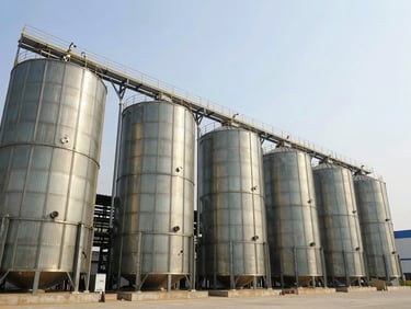 Wide-angle architectural photograph of a modern soy processing facility with massive steel silos under bright daylight, clean industrial lines