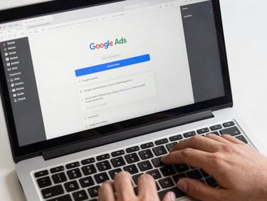 Close-up overhead of a laptop screen displaying a Google Ads campaign interface mid-edit, a hand resting near the keyboard, clean studio lighting with no glare, screen content fully readable