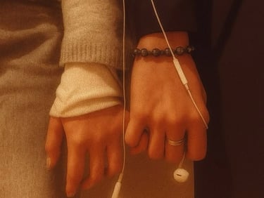 Close-up of a couple's hands touching while sharing white wired earphones in warm lighting.