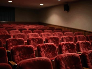 An empty theater hall with red velvet seats seen from the stage, soft ambient light, warm muted tones, cinematic, shallow depth of field.