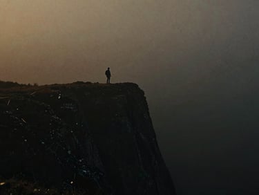 Cinematic wide shot of a solitary figure on a misty, dark cliffside, low-key chiaroscuro lighting, anamorphic lens, 35mm film grain