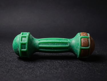 Tough rubber dog chew toy on a dark textured background, dramatic side lighting, rich green accents, 50mm lens