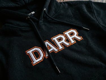Close-up of a premium heavyweight black cotton hoodie with intricate white and orange embroidery