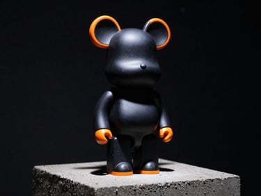 A sleek matte-black vinyl art toy with high-gloss orange accents, standing on a concrete pedestal