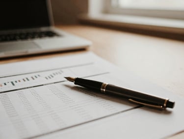 Close-up of a minimalist desktop with financial documents and a fountain pen, soft natural light, muted earth tones, shallow depth of field, warm editorial photography.