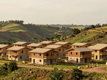 Wide-angle architectural documentary photograph of finished sustainable housing units integrated into a lush green valley, warm overcast daylight, soft earthy tones