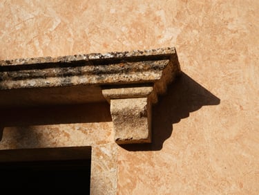 Extreme close-up of a textured lime-plaster wall meeting a raw sandstone lintel, high-contrast tropical sunlight, deep shadows, 35mm
