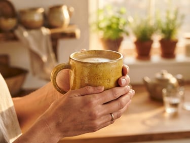 A pair of hands gently cradling a warm, buttery yellow stoneware mug, soft golden-hour window light, shallow depth of field, cozy kitchen background, rich saturated earthy tones.