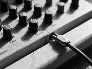 Extreme close-up of a modular synthesizer patch cable plugged into raw, hand-carved Greek marble, high-contrast harsh shadows.