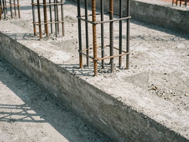 Close-up of freshly poured concrete foundation with rebar, emphasizing texture and structural detail, natural directional daylight.