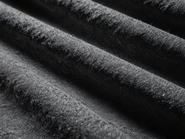 Dramatic close-up of thick, heavy-weave raw grey linen fabric texture, deep folds, high-contrast side-lighting showing individual flax fibers.