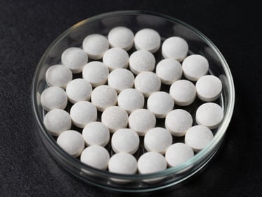 Overhead shot of small white vitamin tablets and mineral crystals, clean laboratory dish, dark background