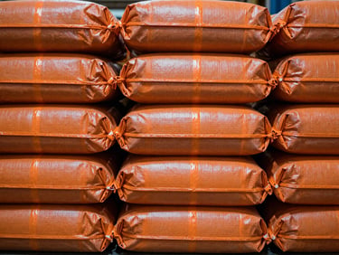 Close-up of neatly stacked rolls of orange Lino woven plastic bags in an industrial warehouse, sharp focus, technical lighting