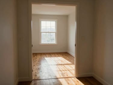Interior doorway of an empty apartment photographed from the threshold, natural daylight streaming through a window at the far wall, hardwood floor detail visible, no people