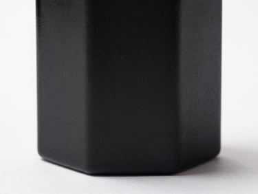 Macro extreme close-up of a luxury perfume bottle mockup, textured matte black glass, sharp studio lighting with deep shadows on a clean white surface.
