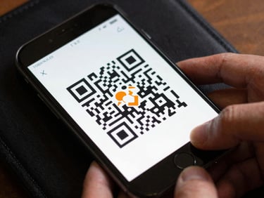 Overhead close-up of a phone screen displaying a QR ticket confirmation, the screen bright against a dark pocket or bag, hands visible at the edges holding the device steady
