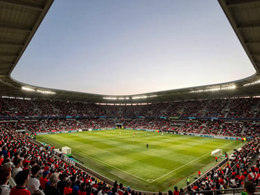 Wide shot of a packed soccer stadium at dusk, floodlights on, crowd in team colors filling the stands, golden light on the pitch