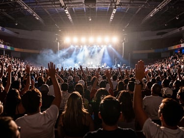Wide-angle view from inside a packed Mexican concert arena, crowd raised hands and stage lights blazing in the distance, natural venue atmosphere, motion blur of energy