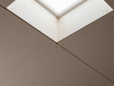 Overhead detail shot of gypsum board ceiling panels joined at seams, screws countersunk at regular intervals, joint compound applied at seams, natural daylight from a north-facing skylight creating even shadowless exposure, no people, tile pattern fills the frame edge to edge