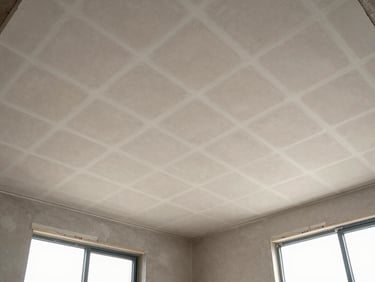 Wide overhead shot of a finished gypsum ceiling grid in an empty room, natural light entering from windows to one side, framing channels and board joints clearly visible from below