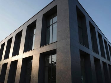 Wide angle architectural shot of a modern building facade with dark grey composite cladding, sharp geometric lines, dramatic afternoon sun.
