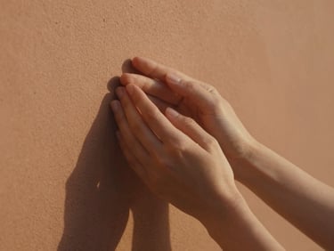 Close-up of hands holding gently against a warm terracotta wall, soft natural golden light, shallow depth of field