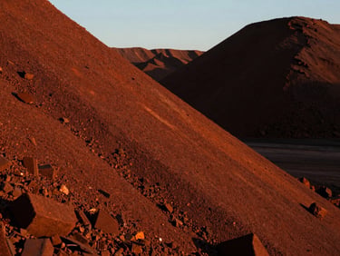 Close-up of processed iron ore stockpiles at golden hour, deep rust-orange texture of high-grade ore, dramatic low-sun angle, high contrast, industrial documentary style, 35mm.