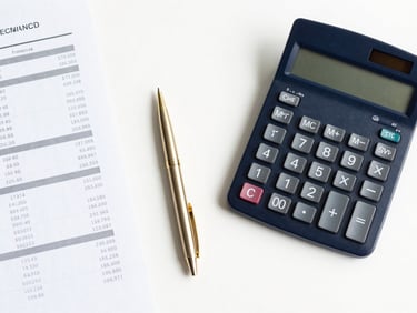 Overhead flat-lay of financial paperwork, calculator, and pen on a clean white desk, gold pen accent, bright shadow-free office lighting, professional corporate photography