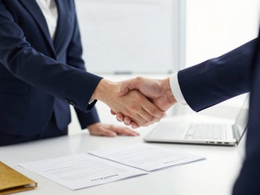 Professional handshake across a formal office desk, loan agreement papers spread open, bright indoor lighting, deep navy and gold stationery, sharp 50mm corporate photography