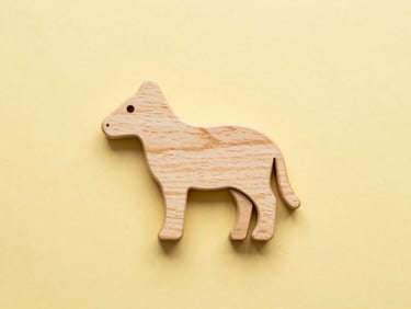 Overhead flatlay of minimalist wooden animal toys with engraved branding on a warm yellow background, crisp studio light, high-key product photography