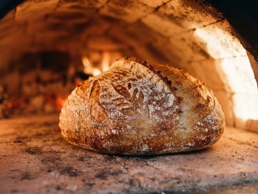 Tight macro architectural crop of a golden-brown sourdough loaf inside a glowing ceramic-interior oven, hard late-afternoon side-light, rich terracotta tones, 35mm