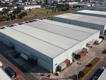 Vista panorámica aérea de un parque industrial moderno en México, naves industriales con techos estructurados, camiones de carga alineados en andenes, luz natural brillante.